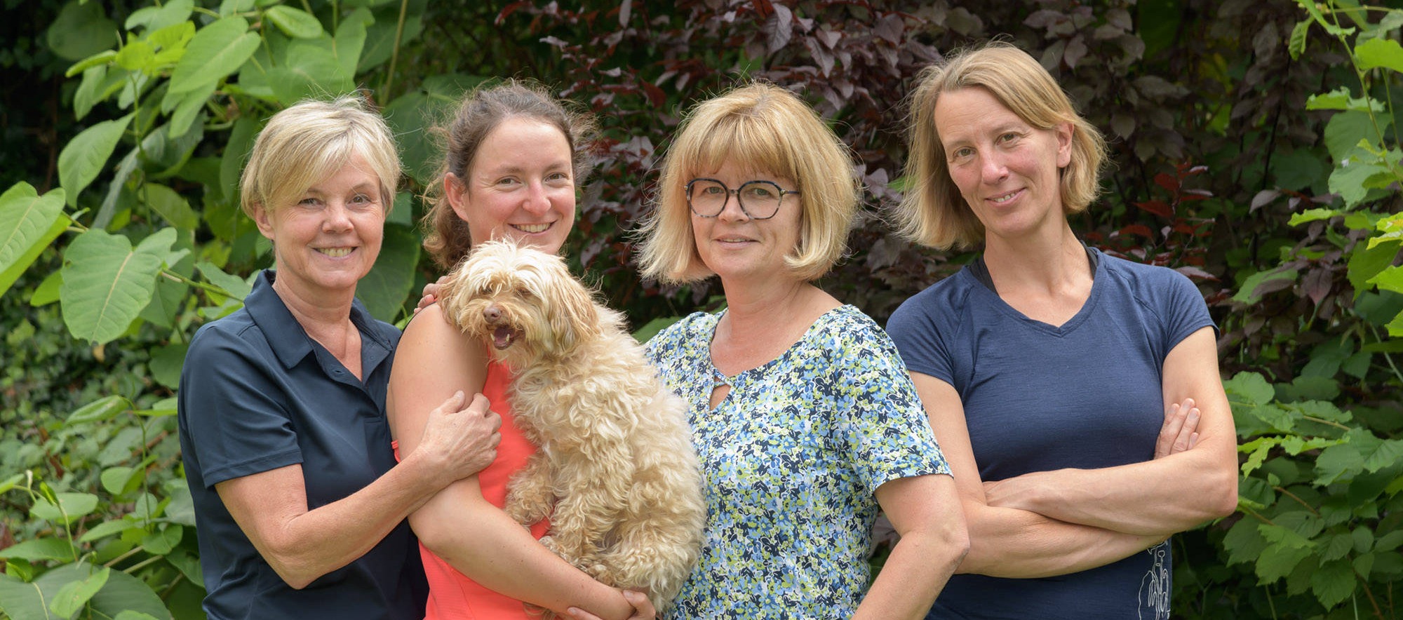 Gruppenfoto des Praxisteams von Sabine Laube: vier Frauen mit einem Hund vor einer begrünten Wand
